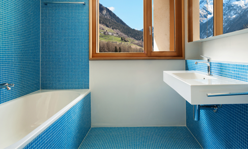 A modern bathroom with blue tiles, white fixtures, and a mountain view.