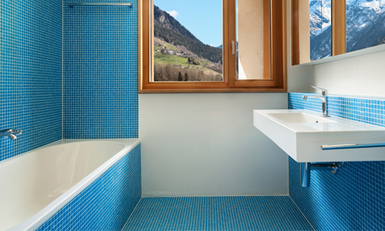 A bathroom with blue tiles, a tub, sink, and a window view of mountains.