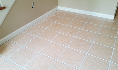 A room corner with newly installed beige floor tiles and an electrical outlet